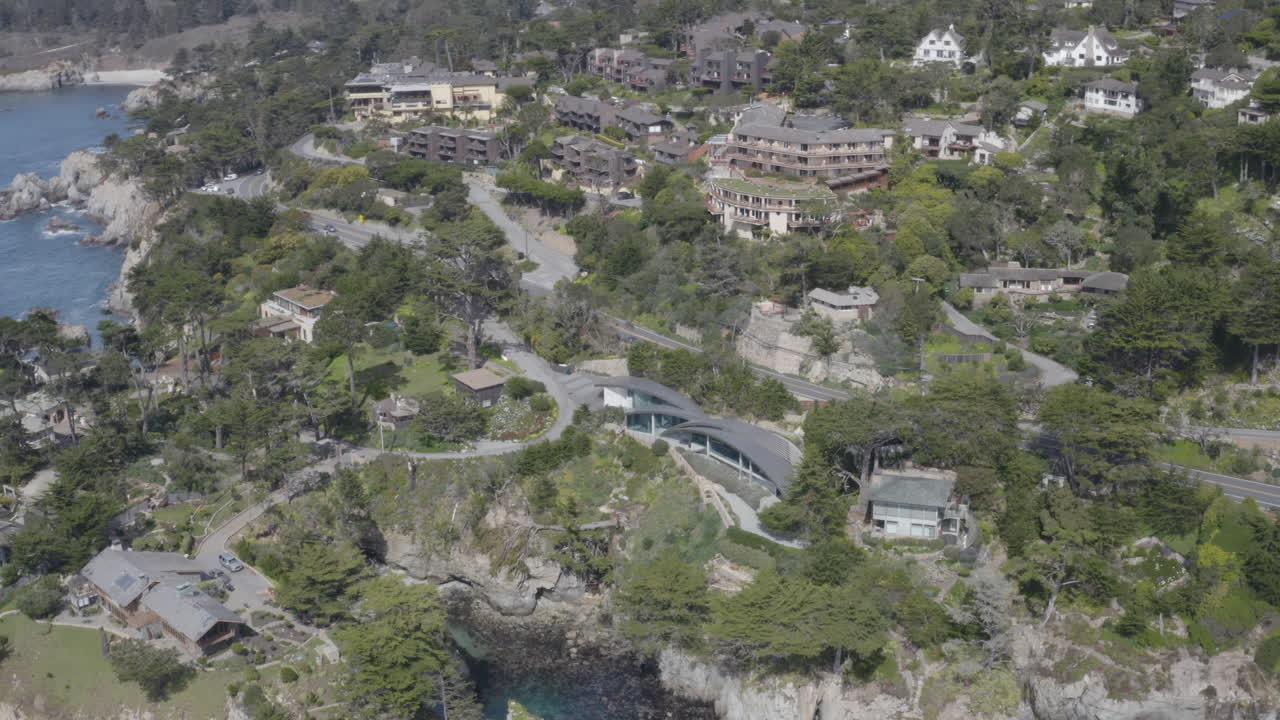 4K aerial view of a cove neighborhood in the Carmel Highlands California bisected by the Pacific Coast Highway..