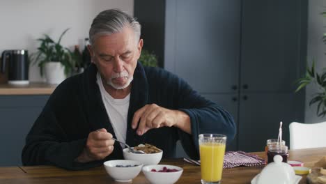 un hombre caucásico mayor desayunando en casa.