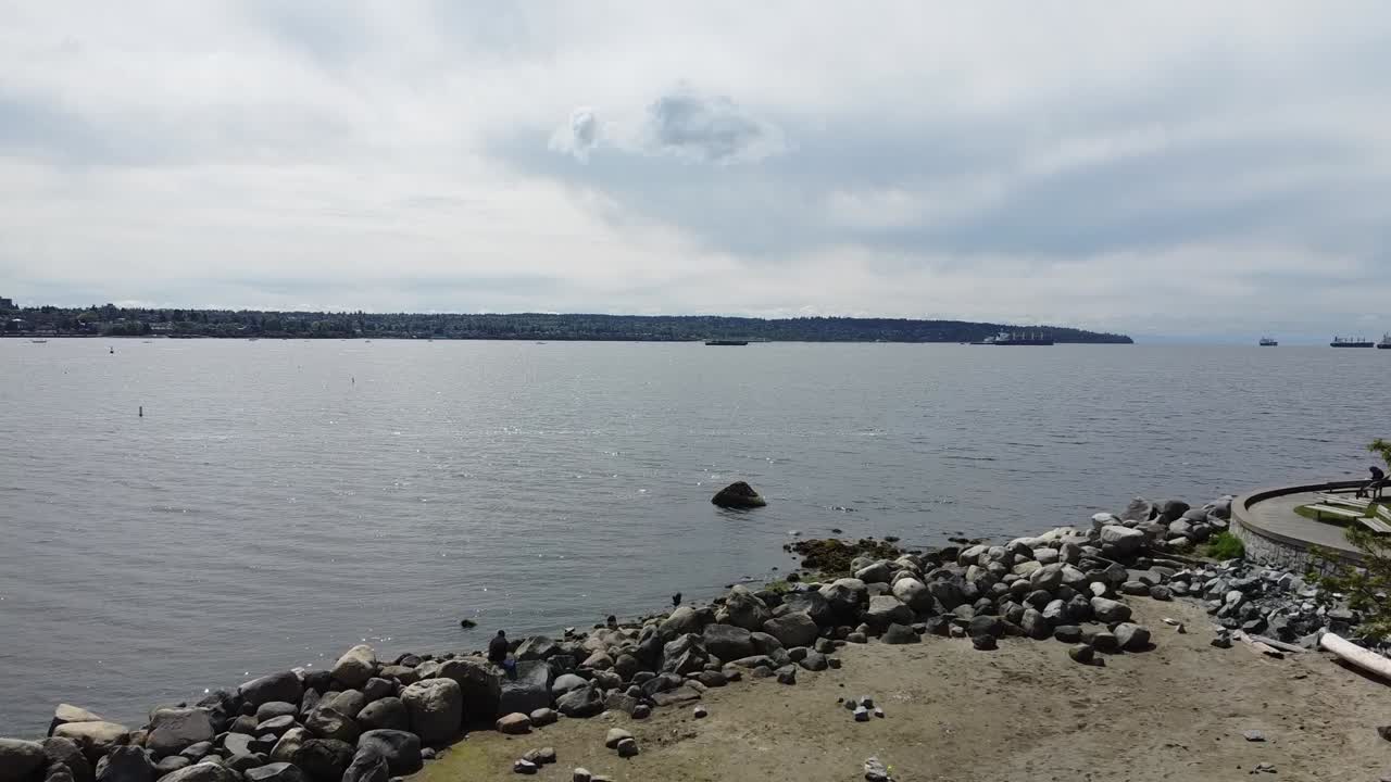 흐린 봄날 방파제 옆에 있는 바위가 많은 썰물 잉글리시 베이 하버 위로 공중 비행하여 아무도 산책하러 나가지 않고 오직 한 사람만 바위 밴시티 bc에서 선탠을 하고 있습니다.