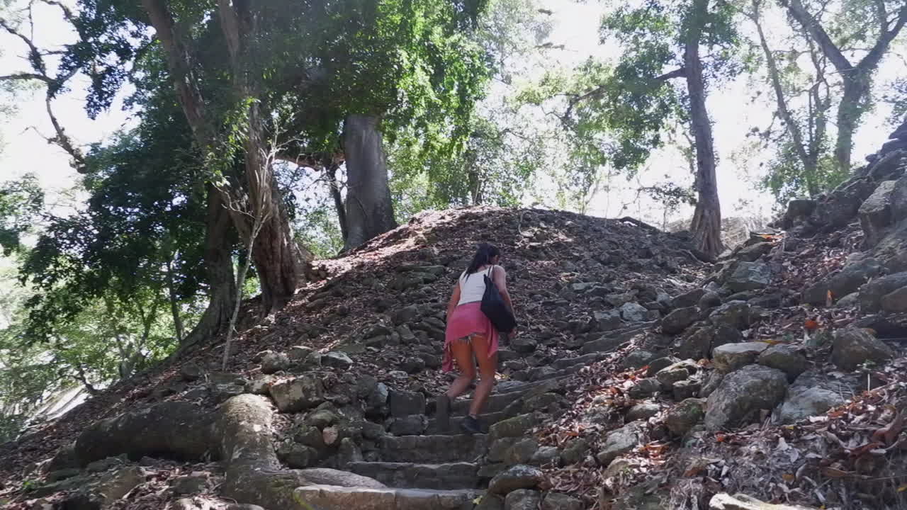 여성 관광객 이 부분적 으로 발굴 된 마야 코판 유적 에서 돌 계단 을 오르고 있다