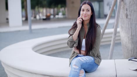 Junge-Frau-Sitzt-Mit-Einem-Mobiltelefon-Auf-Einer-Wand