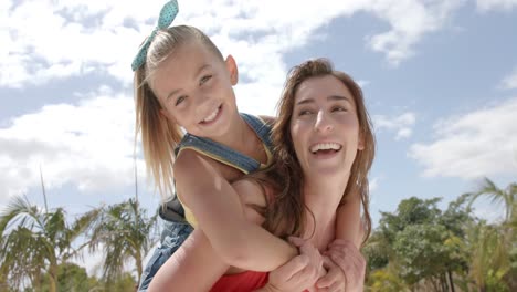 retrato de una madre caucásica feliz llevando a su hija sobre las palmeras