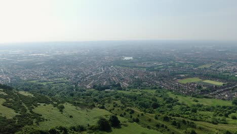 Aerial-drone-shot-over-hills-with-meadows-and-forests-with-view-of-a-city-and-haze-on-horizon