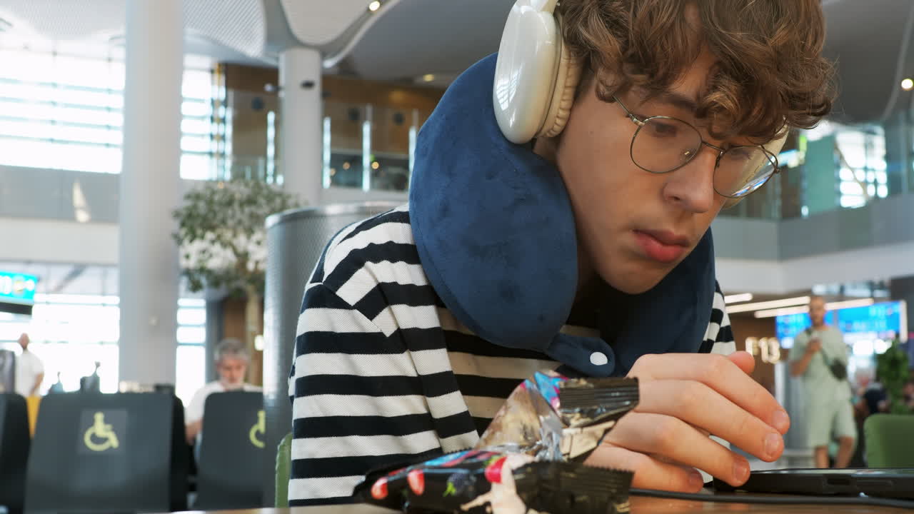 Young Man with Headphones and Neck Pillow Using Phone in Airport
