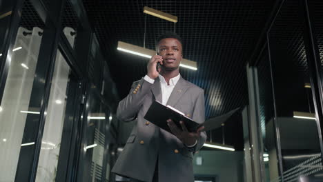a black man is talking on the phone and walking down the corridor with documents