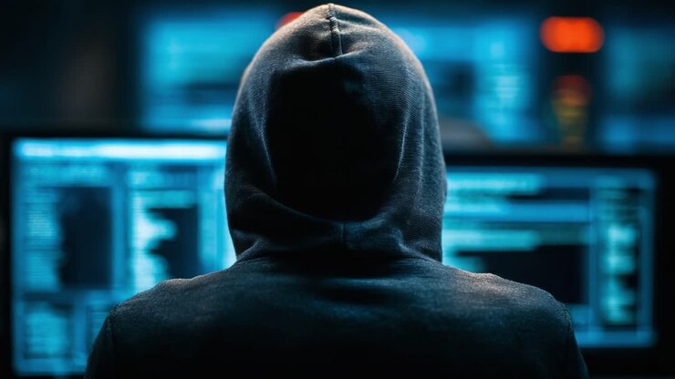 Una figura misteriosa con una felpa con cappuccio si dedica ad attività digitali, circondata da schermi che mostrano flussi di codice, evocando un senso di intrigo e suspense in un ambiente oscuro
