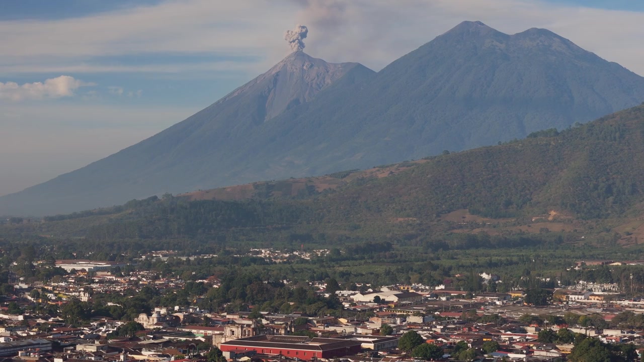 Aktive Volcán de Fuego udspyr aske og røg med byen Antigua, Guatemala i forgrunden.