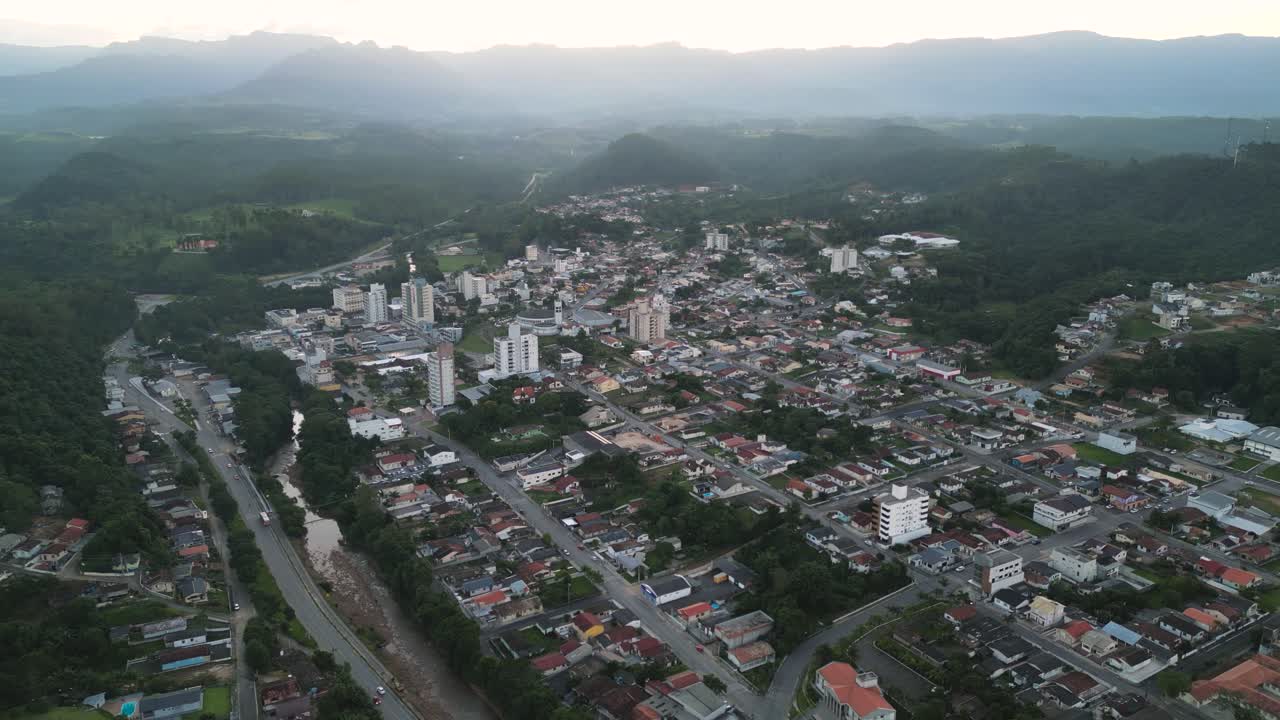 Wide aerial shot showcasing the urban area of Lauro Muller, Santa Catarina, Brazil, surrounded by mountains and a river, highlighting the city's connection to nature and its geographic location