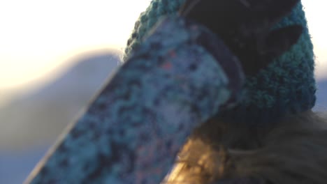 attractive blonde woman puts winter hat on, golden sunset, backlight, closeup