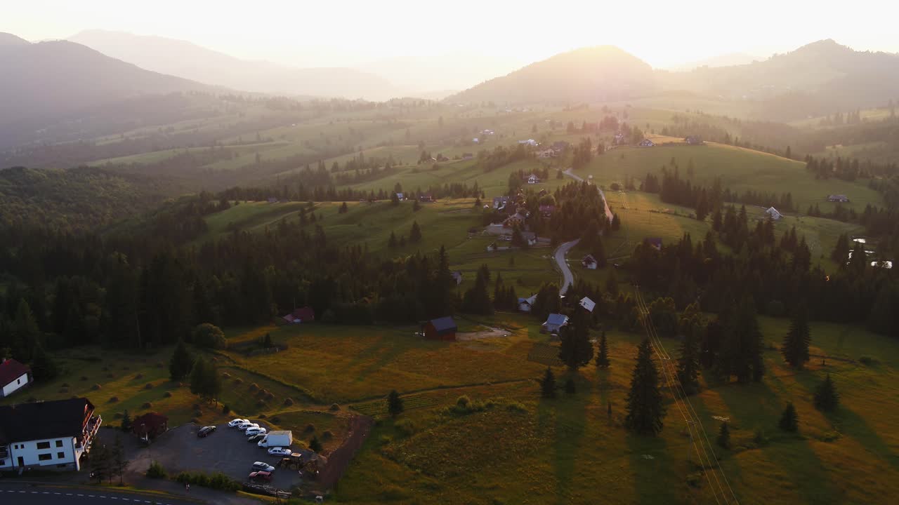 Wide aerial shot of a rural village, Colibita, Bistrita Nasaud, nestled in rolling green hills and forests during golden hour