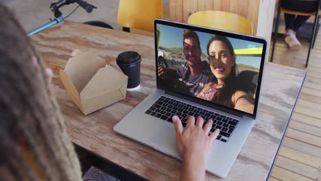 Mixed-race-man-sitting-in-cafe-using-laptop-making-video-call-with-friends