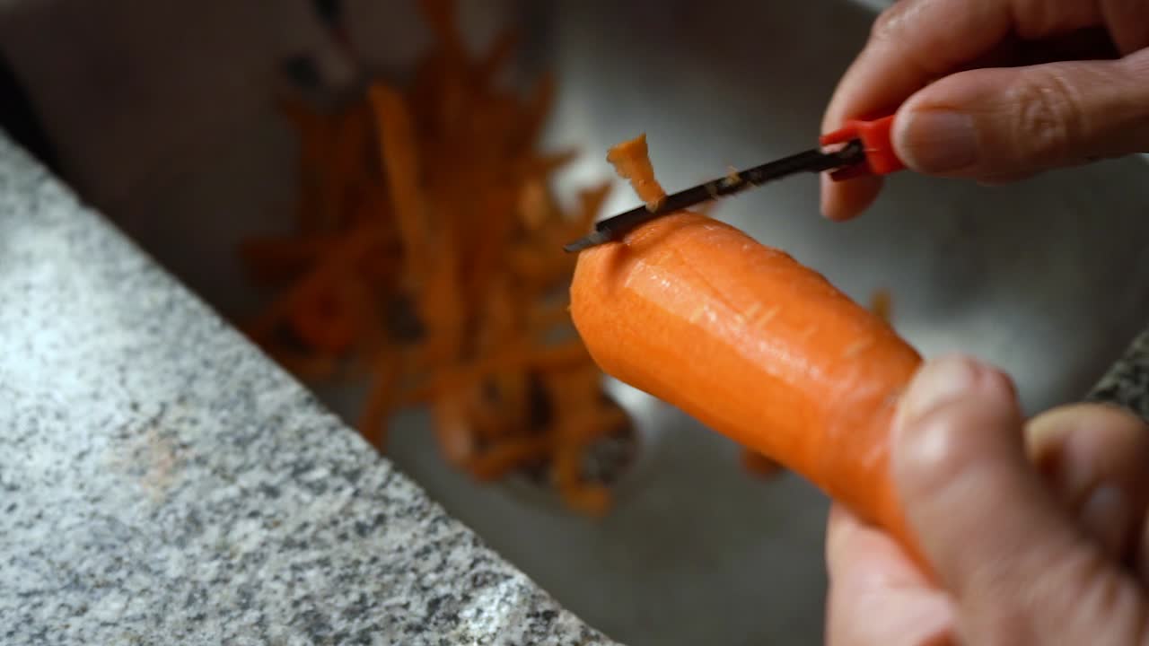 Woman Peeling The Fresh Carrot On The Stainless Kitchen Sink - close up, selective focus
