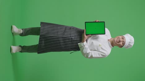 full body of asian man chef smiling and showing green screen tablet to the camera while standing in the green screen background studio