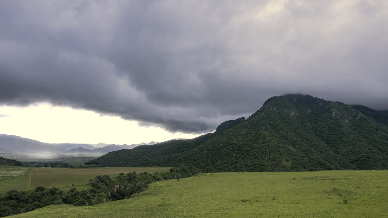거대한 언덕이 있는 넓은 초록색  ⁇ , 대조적인  ⁇ 빛과 왼쪽의 폭풍, 빠르게 움직이는 구름이 언덕과 충돌하고 주변을 둘러싸고, 속도와 움직임의 감각을 만 ⁇ 니다.