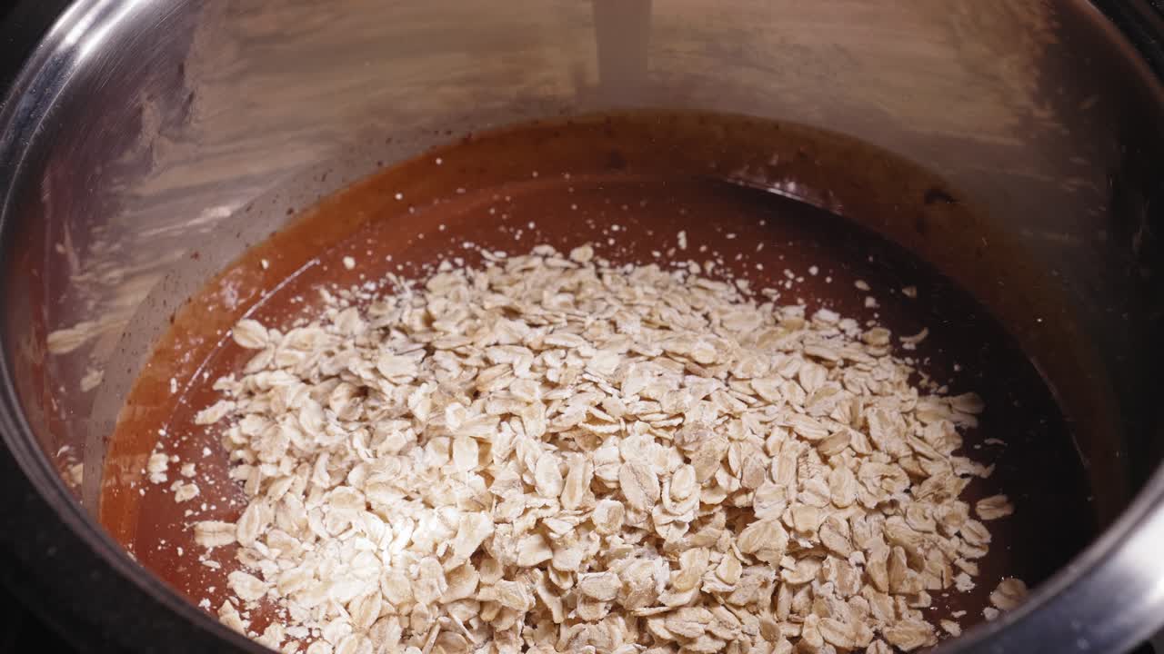 agregando copos de avena, polvo de proteína de suero y semillas de chía en una olla con leche de coco y mezcla de chocolate amargo derretido