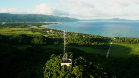 scenic aerial drone shot of telecommunications tower atop lush hill overlooking tropical island village coastline at virac, catanduanes, philippines.