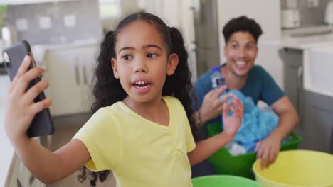 Happy-biracial-father-and-daughter-making-video-call-using-smartphone,-sorting-waste-together