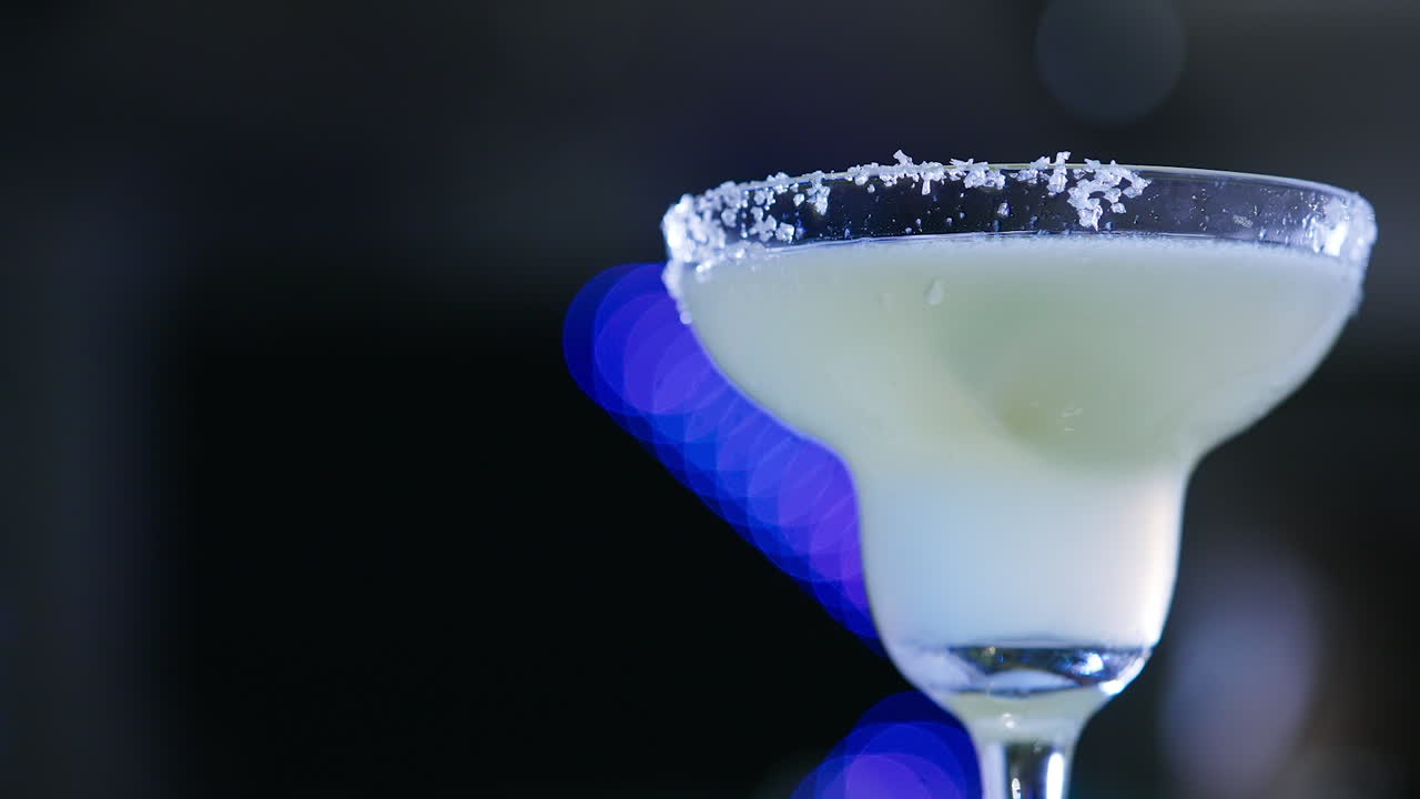 Margarita glass with white beverage. Glass top decorated with crystals of salt. Close up. Blurred backdrop.