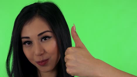 young attractive asian woman shows thumb on agreement - green screen - closeup
