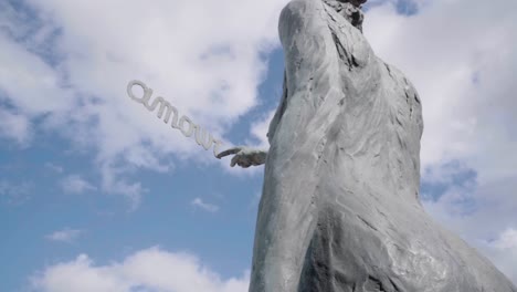 Escultura-De-Mujer-Escribiendo-La-Palabra-Francesa-Amour-En-El-Cielo-Por-El-Escultor-Belga-Linde-Ergo-En-De-Haan,-Mar-Del-Norte,-Bélgica---ángulo-Bajo