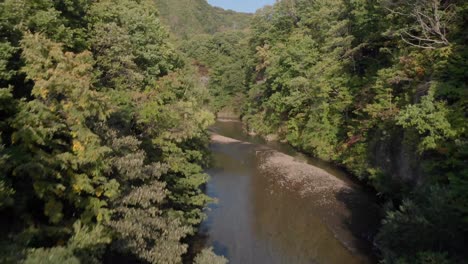 Aerial-shot-slowly-rising-and-tilt-reveal-of-mountainous-scenery-above-dense-green-forest-and-river-in-Jozankei-famous-onsen-hot-spring-town-Hokkaido,-Japan