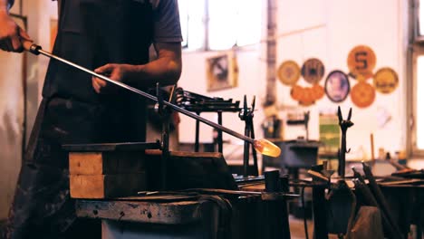 Mid-section-of-glassblower-shaping-a-molten-glass