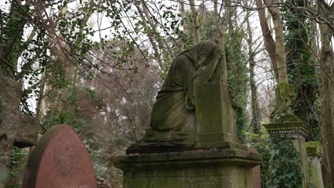 praying statue on a gravestone covered in moss in a forest cemetery on a cloudy day