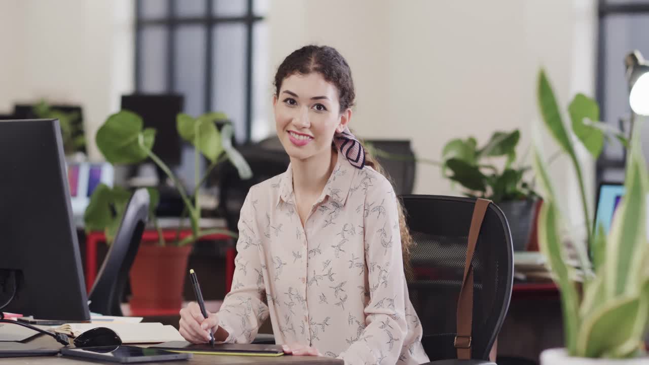 feliz mujer biracial creativa usando una tableta en una oficina casual, en cámara lenta