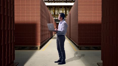 full body side view of an asian male professional worker with red brick packed in stacks are stored, observes by looking up before he come to concentrating on the laptop and keep on typing