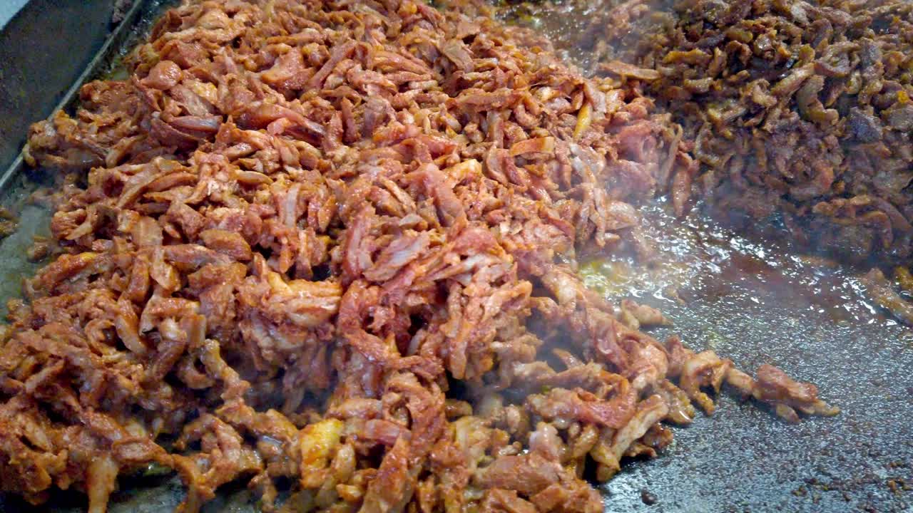 Close up of seasoned meat sizzling on a hot griddle with visible steam and rich texture