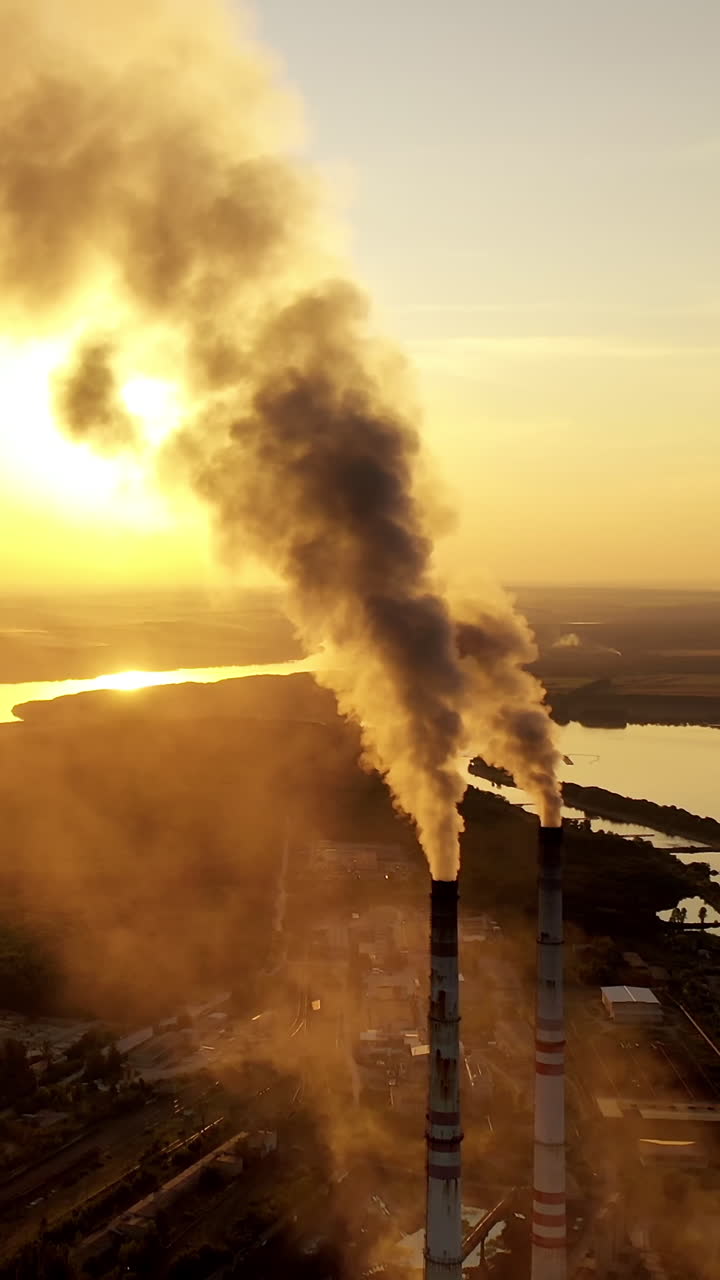 Smoking factory chimney. Plant emits smoke and smog from the pipes at sunset, pollutants enter the atmosphere. Vertical video