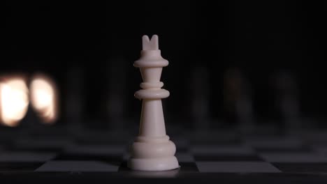 close-up of a white king standing alone on a chessboard with the other pieces off in the dark