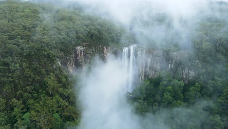 looking through a mist covered mountain revealing a majestic waterfall descending into a tropical rainforest below