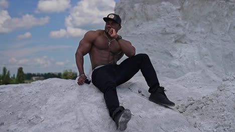 thoughtful black skinned guy sitting on white stone. shirtless african american man with muscular body rests outdoors. sportsman on hill in summer.
