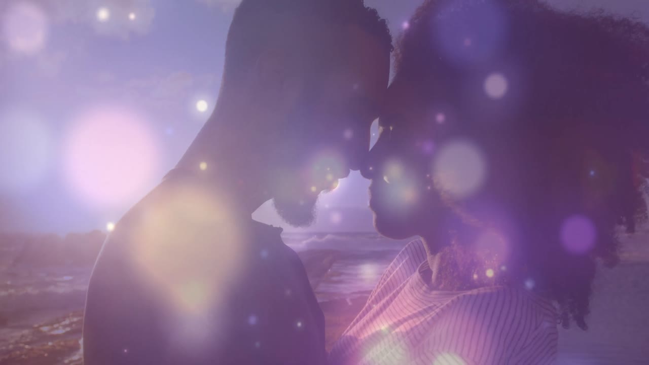 아프리카계 미국인 부부 위에 빛나는 파란색 반점이 바다 근처의 바위에서 서로 포옹하고 있습니다.