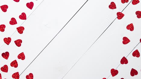 Vlentine's-Day-composition--Heart-shaped-sequins-placed-on-white-wooden-table
