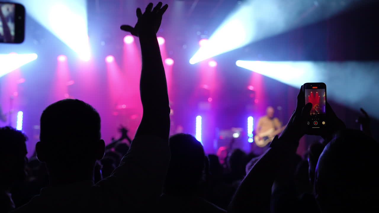 Energetic concert crowd recording live performance, holding smartphones high and capturing vibrant music festival atmosphere with passionate enthusiasm