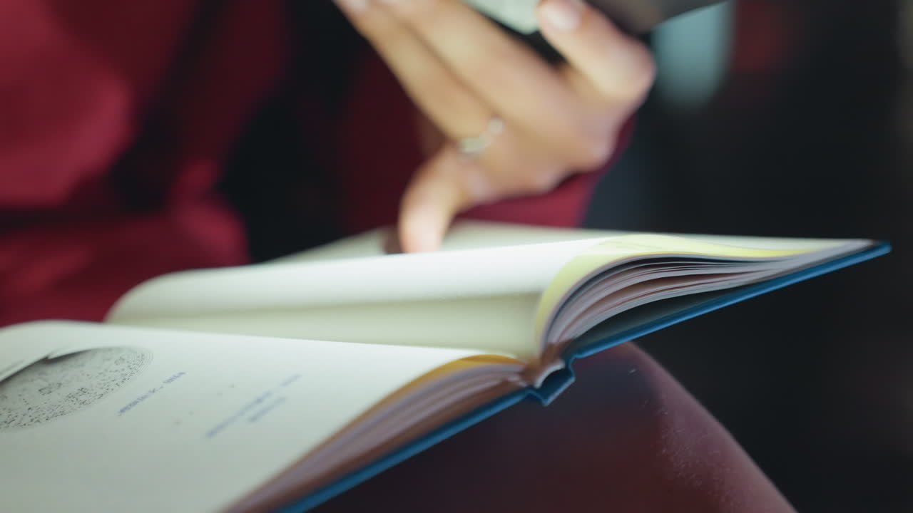 Nahaufnahme einer Person, die Notizbuchseiten umblättert. Hände in einem roten Pullover blättern langsam durch ein blaugebundenes Notizbuch, während ein beringter Finger kurz am Seitenrand verweilt. Sanftes, warmes Licht und eine geringe Tiefenschärfe erzeugen eine gemütliche, nachdenkliche Atmosphäre.