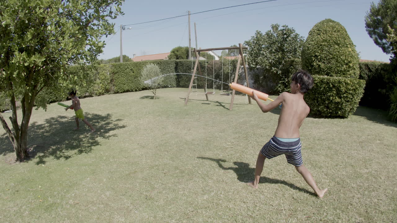 dos chicos luchando con armas de agua en el patio trasero en un día soleado.
