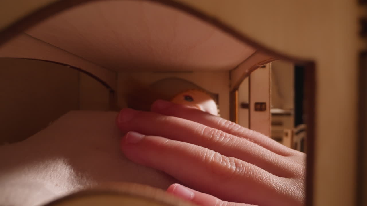 Little girl touches and adjusts fabric on dolly in toy house