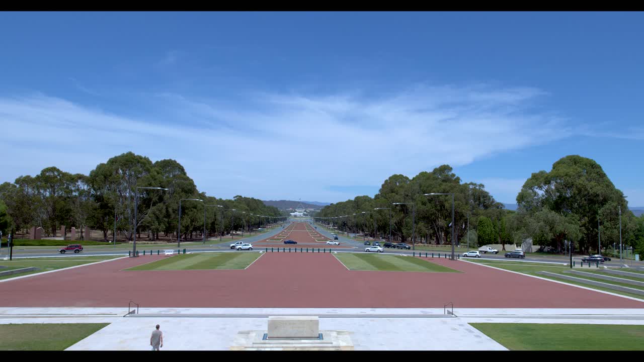 Ampia inquadratura statica di Anzac Parade che conduce al Parlamento sotto un cielo blu brillante