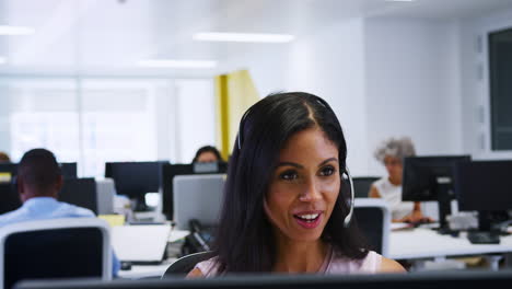 Young-woman-working-at-computer-with-headset-in-busy-office