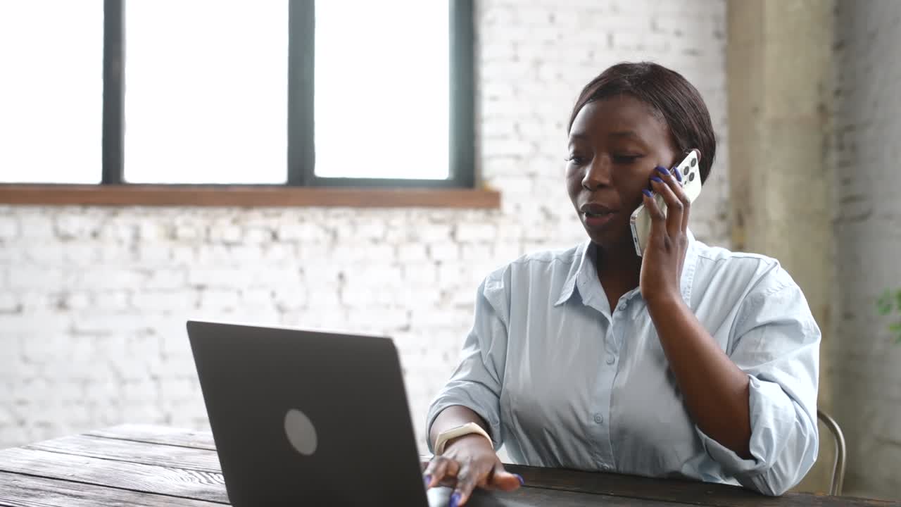Imprenditrice afroamericana impegnata che parla al telefono e usa il laptop.