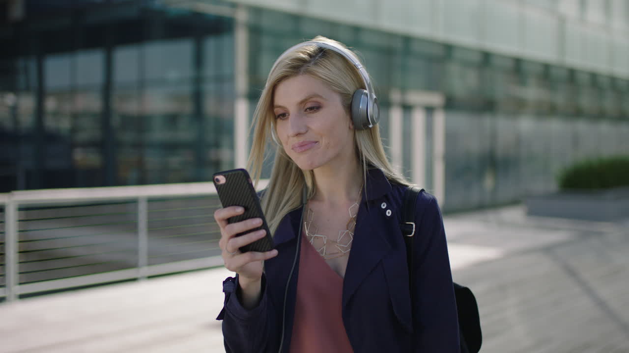 ritratto di una giovane donna d'affari bionda e vivace che si diverte ad ascoltare musica indossando cuffie, inviando messaggi, navigando sui social media utilizzando uno smartphone