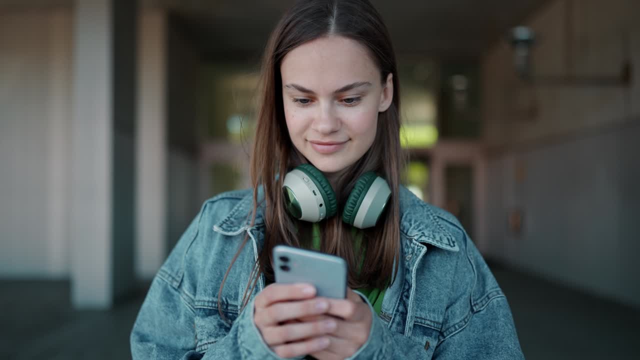 mujer positiva con auriculares escribiendo por teléfono
