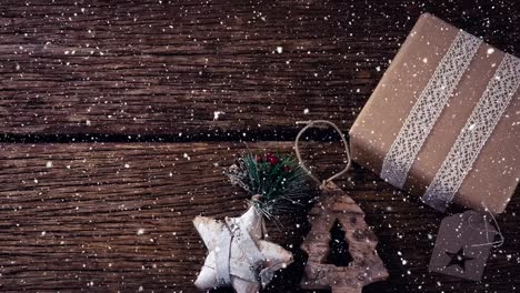 Fallender-Schnee-Mit-Weihnachtsdekorationen-Und-Geschenk-Auf-Holz