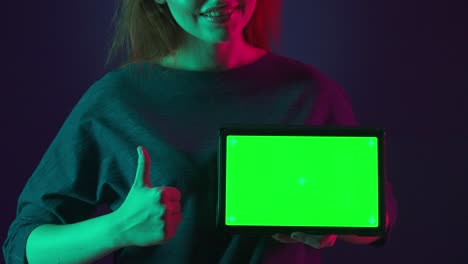 woman holding tablet with green screen under neon lighting