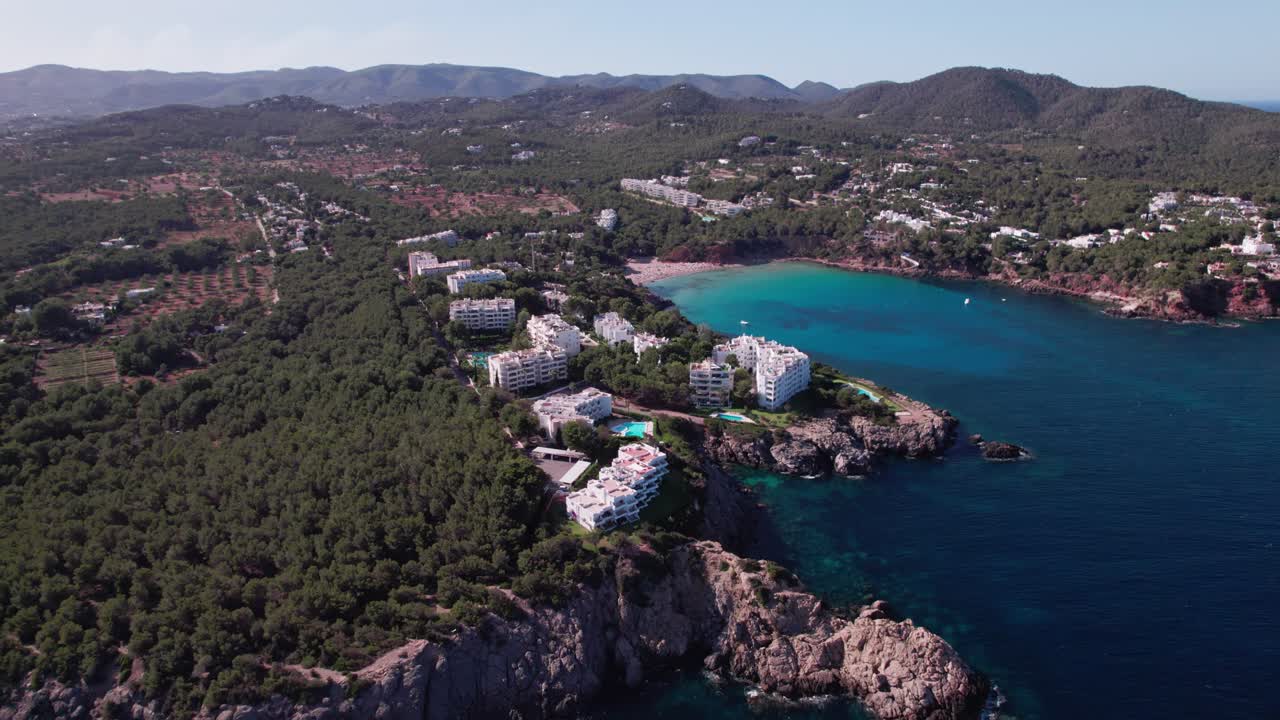 vuelo de drones en un acantilado cerca de una playa con árboles y casas en la isla de ibiza en españa