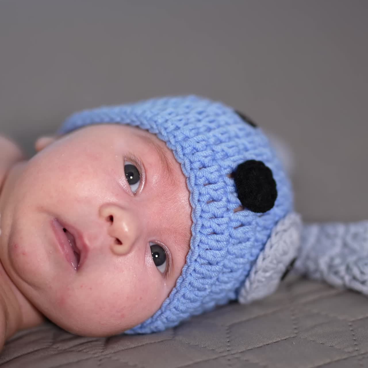 Small kid lying and moving his tiny hands quickly. Adorable babe in funny blue doggy cap and knitted bone. Beautiful child in the bedroom
