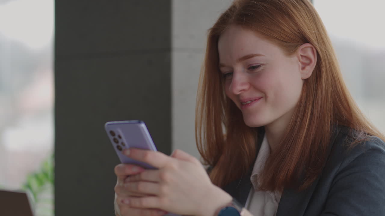 Beautiful young business woman using phone in office. Woman using a smartphone and leaning on a window texting sending emails planning meetings networking online browsing messages on mobile phone